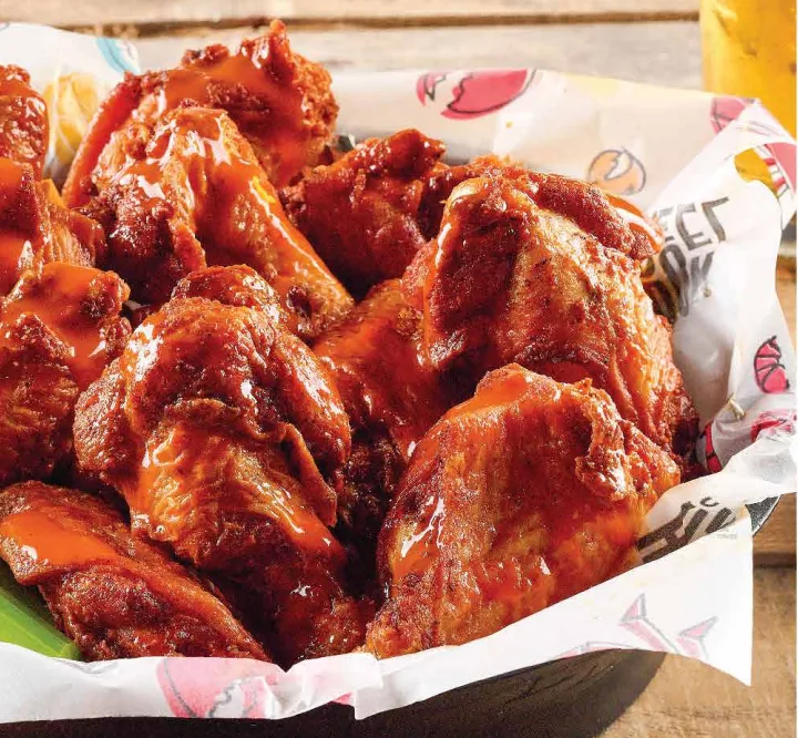 A basket of saucy chicken wings with celery and a cup of dressing
